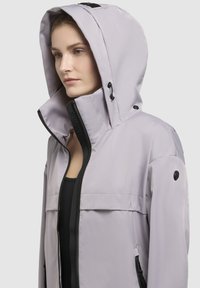 Light gray jacket with a high collar and large hood, featuring black zippers and accents. Smooth, water-resistant fabric, minimalistic design.