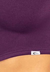 Lilla ribbet crop top med en tætsiddende pasform, blød tekstur og et lille hvidt mærke med et sort logo ved kantet.