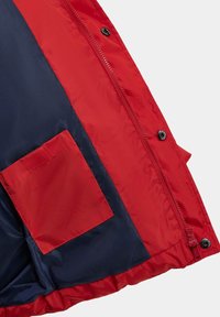 Interieur van een rood en marineblauwe gewatteerde jas met ritsluiting, drukknoopjes en een zichtbare zak aan de linkerkant. Glad, glanzend materiaal.