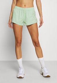 Shorts deportivos de color verde claro con cinturilla elástica, tejido suave y corte relajado, combinados con zapatillas deportivas blancas y calcetines.