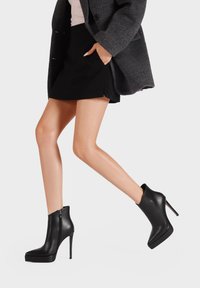 Stivaletti in pelle nera con punta affilata, alto tacco a stiletto e zip laterale; design elegante con suola a piattaforma per un'altezza extra.