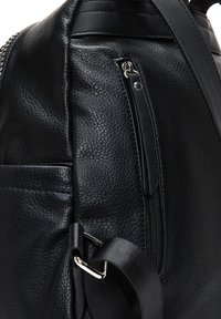 Sac en cuir noir avec une finition texturée, doté d'une poche latérale zippée et d'une large bandoulière. Accents en métal argenté visibles.