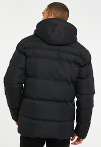 Chaqueta de plumas negra con capucha, con costuras horizontales y un acabado texturizado. La vista trasera muestra un ajuste cómodo y relajado.