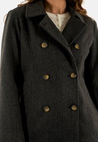 Cappotto doppio petto grigio scuro con colletto a dente, due grandi bottoni marroni e un morbido tessuto in lana testurizzata.