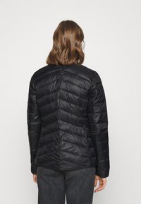 Svart pufferjacka med ett chevron-quiltat mönster, lätt material, rund hals och en mjuk textur. Bakvy utan synlig hårdvara.