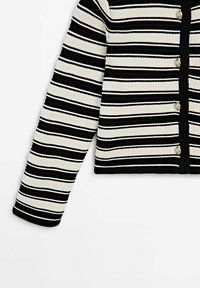 Cardigan en maille rayé horizontal noir et blanc avec manches longues et boutons argentés sur le devant.