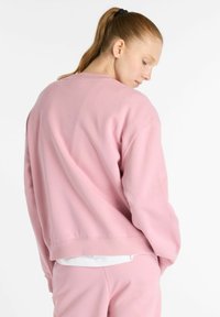 Un sweat-shirt rose avec une coupe décontractée, un col rond, des poignets et un ourlet côtelés. Texture douce, présenté de l'arrière, assorti à un bas coordonné.