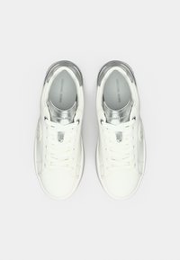 Λευκά δερμάτινα αθλητικά παπούτσια με ασημένιες λεπτομέρειες· διαθέτουν στρογγυλή μύτη, κορδόνια και γυαλιστερή υφή στη γλώσσα και στη φτέρνα. Λείο πέλμα.