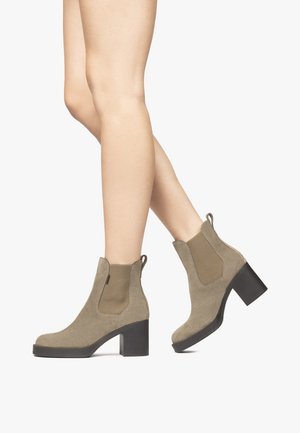 Beige Wildleder-Ankle Boots mit elastischen Seiteneinsätzen und klobigen schwarzen Absätzen. Das Design zeichnet sich durch eine glatte Textur und Zuglaschen für ein einfaches An- und Ausziehen aus.