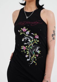 Schwarzes, geripptes Tanktop mit buntem Floral- und Panther-Stickerei sowie metallischen Akzenten, Markenlogo in einer stilisierten Schrift über dem Design.