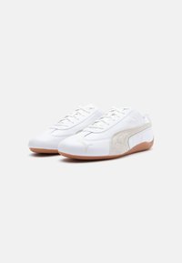 Baskets de sport blanches en matériau synthétique lisse, avec des accents en suède contrastés, design à lacets et semelle en caoutchouc gomme. Détails d'emblème.