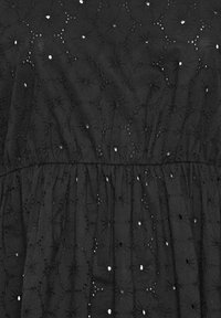 Robe en tissu noir avec broderies complexes de motifs circulaires et découpes œillets, cintrée à la taille pour une silhouette fluide.