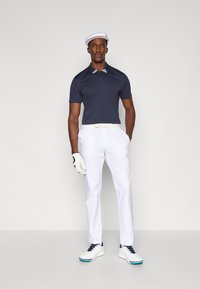 Granatowa koszulka polo z białymi paskami na kołnierzyku, białe spodnie, biały kapelusz i białe buty golfowe z niebieskimi akcentami; teksturowana tkanina i dopasowany krój.