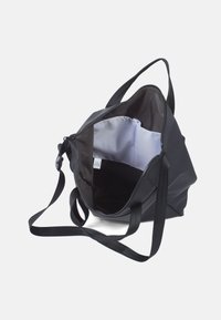 Zwarte totebag van glad, duurzaam materiaal, met een ritssluiting, een open interieur met een lichte stofvoering en zijzakken.