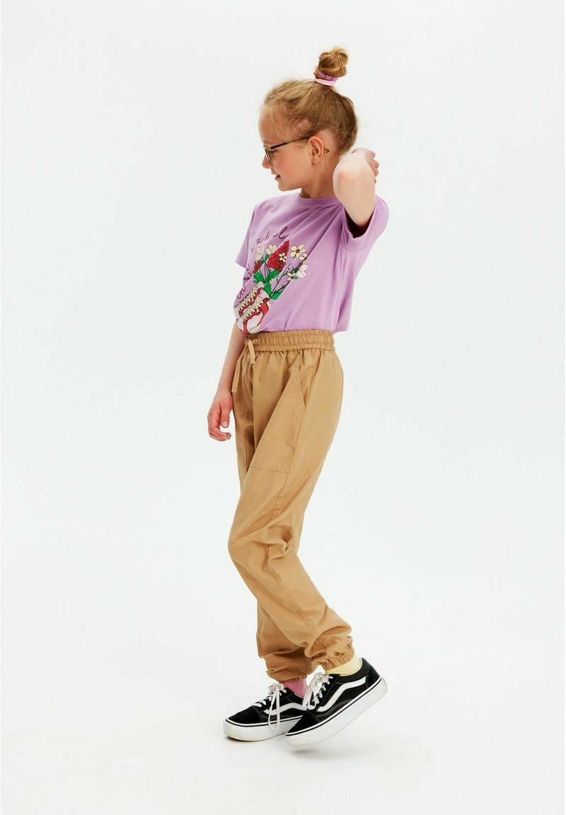 Lavendel t-shirt med blomster grafikdesign, beige tapered bukser og sorte sneakers med hvide såler. Har elastisk talje og manchetter.