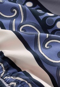 Tissu doux avec des motifs tourbillonnants bleus et blancs et des contours noirs, montrant des plis et des détails de couture froncée.