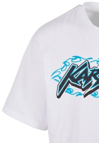 Balts kokvilnas T-krekls ar melnu un zilu grafisko logotipu, kas satur stilizētu tekstu un liesmu motīvus krūšu rajonā. Īsas piedurknes un apaļš kakls.