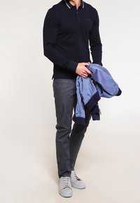 Marinblå långärmad polo med vit rand på kragen, kombinerad med grå jeans och en ljusblå bomberjacka. Vita sneakers fulländar outfiten.