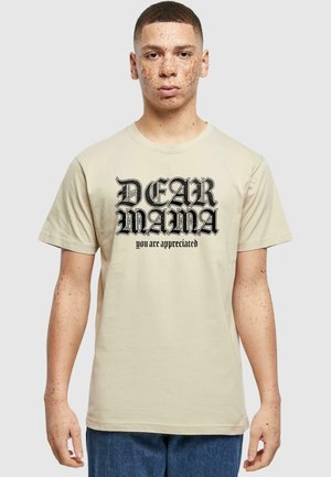 Beige bomulds t-shirt med korte ærmer, der har sort grafisk tekst "KÆRE MOR" og "du bliver værdsat" i fed, dekorativ skrifttype.