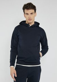 Granatowy hoodie wykonany z gładkiego materiału, z kapturem na sznurki, przednią kieszenią i zamkiem błyskawicznym z boku, z małym logo na piersi.