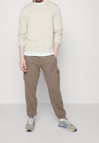 Beige sweatshirt, brown cargo pants, and green sneakers with blue accents. Smooth fabric, relaxed fit, and cargo pockets on pants.