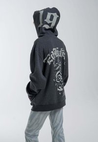 Gray hoodie with a dragon and rose graphic on the back, featuring the number "19" on the hood. Paired with light gray striped pants.