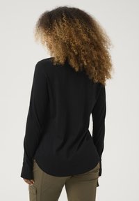 Schwarzes Langarmshirt mit abgerundetem Saum, aus weichem Material, kombiniert mit olivgrünen Cargo-Hosen. Minimalistisches Design ohne sichtbare Logos.