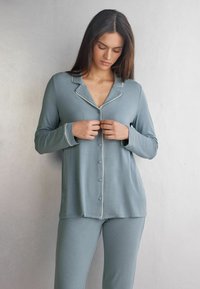 Lichtblauwe pyjama set met een button-up top en bijpassende broek, gemaakt van zacht materiaal met witte bies langs de kraag en manchetten.