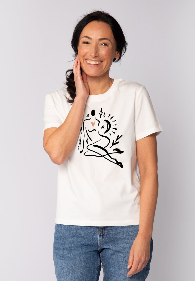 T-shirt en coton blanc avec une illustration abstraite noire et pêche d'une figure assise entourée d'étoiles et de plantes, col rond et manches courtes.