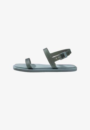 Minimalistisk grå sandal med to stropper, en over tæerne og en rundt om anklen med spænde, flad sål, Calvin Klein-mærke synligt på stroppen.