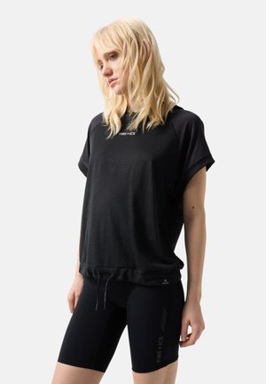 Blonde woman wearing a loose black short-sleeve shirt and fitted black shorts with "FIRE + ICE" logos on both garments.