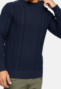 Knitted navy blue pullover sweater with textured patterns, ribbed cuffs and hem, featuring a crew neckline and a fitted silhouette.