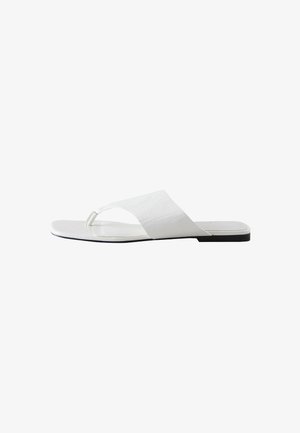 Sandalia plana blanca con una tira ancha y un lazo para el dedo, con suela negra y diseño minimalista.