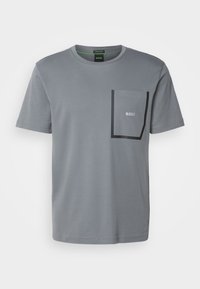 T-shirt gris à manches courtes avec col rond, poche poitrine bordée de noir et petit logo blanc "BOSS" à l'intérieur de la poche sur le côté gauche.