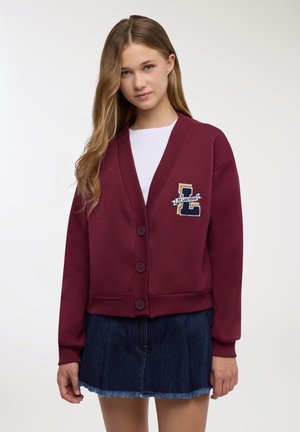 Cardigan color bordeaux con scollo a V, chiusura con bottoni e toppa con la scritta "St. Las Vegas." Abbinato a una minigonna in denim. Tessuto liscio.