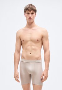 Μπεζ μπόξερ με λεία υφή και ελαστική μέση. Ο σχεδιασμός είναι εφαρμοστός, καλύπτει μέχρι το μέσο του μηρού και διαθέτει διαμορφωμένη θήκη.