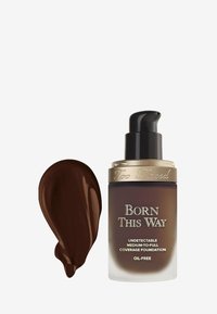 Bruine glazen foundationfles met een gouden pompdeksel. Het etiket zegt "Born This Way" in goud, omringd door een donkere foundation swatch.