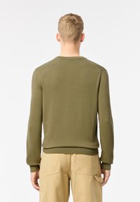 Suéter de punto verde oliva con puños y dobladillo acanalados, escote redondo y una textura suave, mostrado desde la parte de atrás sobre un fondo neutro.