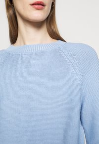 Ljusblå stickad tröja med rund halsringning, texturerat mönster och raglanärmar. Mjukt material med ribbad krage.