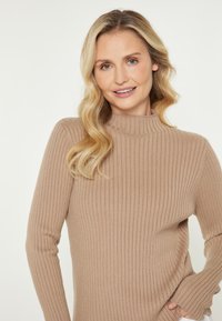 Beige Rippenstrickpullover mit hohem Hals, langen Ärmeln und weicher Textur, der eine taillierte Passform hat und den Körper contours.