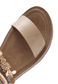 Flat sandal with a wide metallic gold strap, a tan footbed, and decorative multi-colored embellishments along the side. Smooth texture.