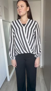 Svart-hvitt stripet bluse med lange ermer, v-hals og innviklet design. Kombinert med svarte vide bukser.