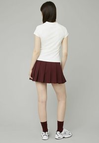 Haut blanc à manches courtes assorti à une jupe plissée bordeaux. L'ensemble présente un design ajusté et la jupe a une texture superposée.