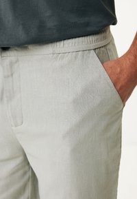 Světle šedé kalhoty s volným střihem, elastickým pasem a bočními kapsami; látka působí měkkým a mírně strukturovaným dojmem.