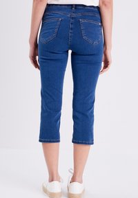 Blauwe cropped jeans met een aansluitend ontwerp, achterzakken en een zoom net onder de kuit. Draag met witte platform schoenen.