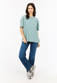 Lichtgroen oversized T-shirt met korte mouwen en een ronde halslijn, gecombineerd met blauwe jeans en grijze sneakers. Eenvoudig, casual ontwerp.