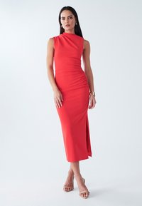 Sarkana pieguļošā midi kleita ar vienu atsegto plecu, sasmērētu sānu detaļu un augstu šķēlumu. Gluda auduma, minimālistisks stils.