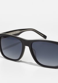 Ochelari de soare din plastic negru, cu lentile gradient albastre, design unghiular și brațe drepte. Fără logo-uri sau accente suplimentare vizibile.