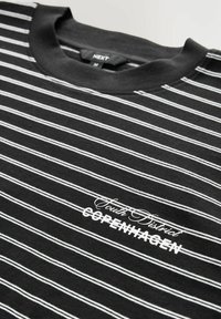 Sort t-shirt med vandrette hvide striber, med rund hals og teksten "South District COPENHAGEN" i hvid, placeret centralt.