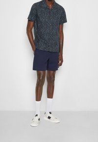 Koszulka z krótkim rękawem w czarnym kolorze z niebieskim abstrakcyjnym wzorem, zestawiona z granatowymi szortami. Noszona z białymi skarpetkami oraz sportowymi butami z akcentami w kolorze granatowym.